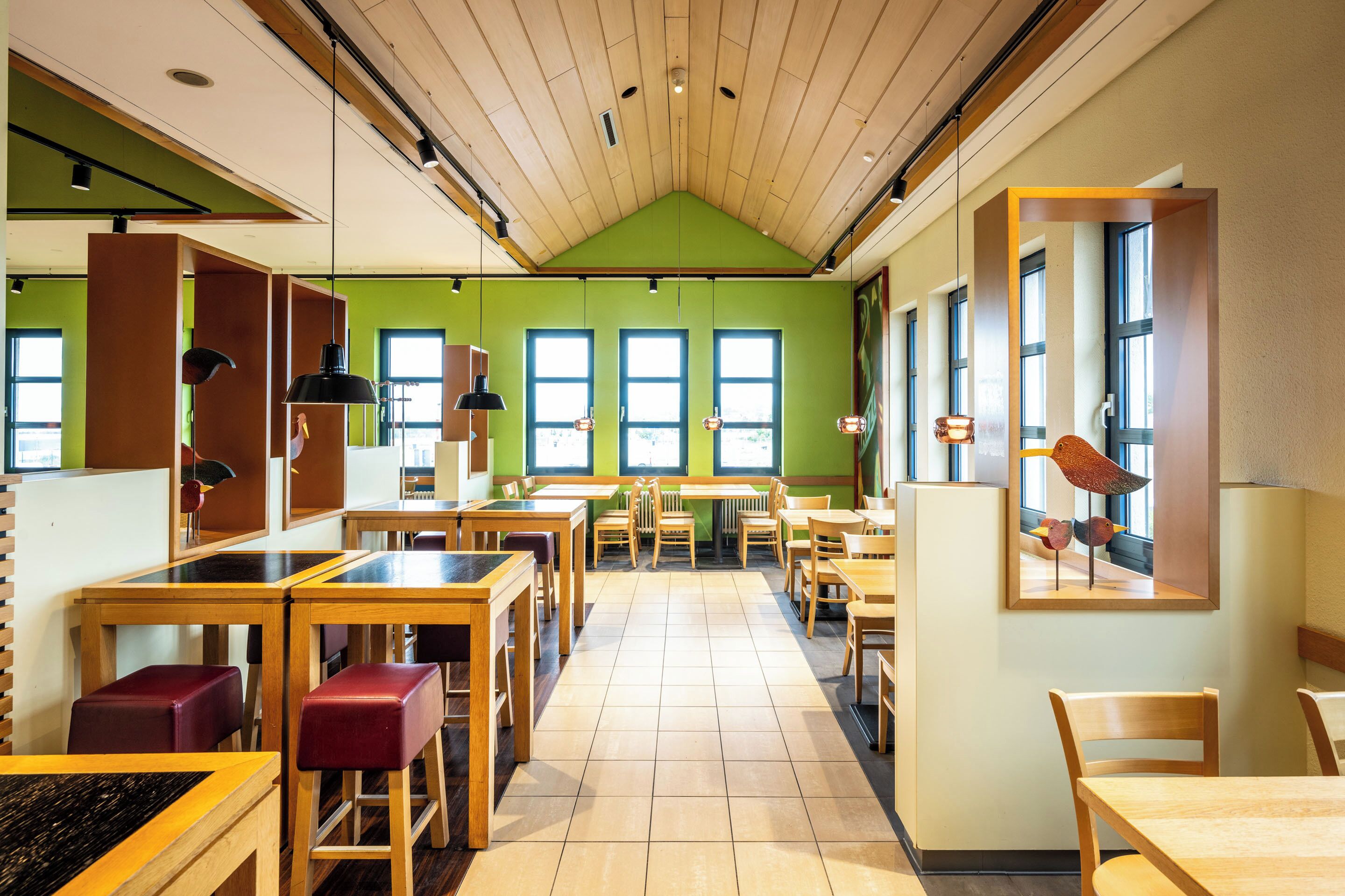 A restaurant with wooden tables and chairs, green walls, and large windows.