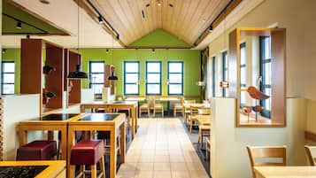Un restaurante con mesas y sillas de madera, paredes verdes y ventanas amplias.