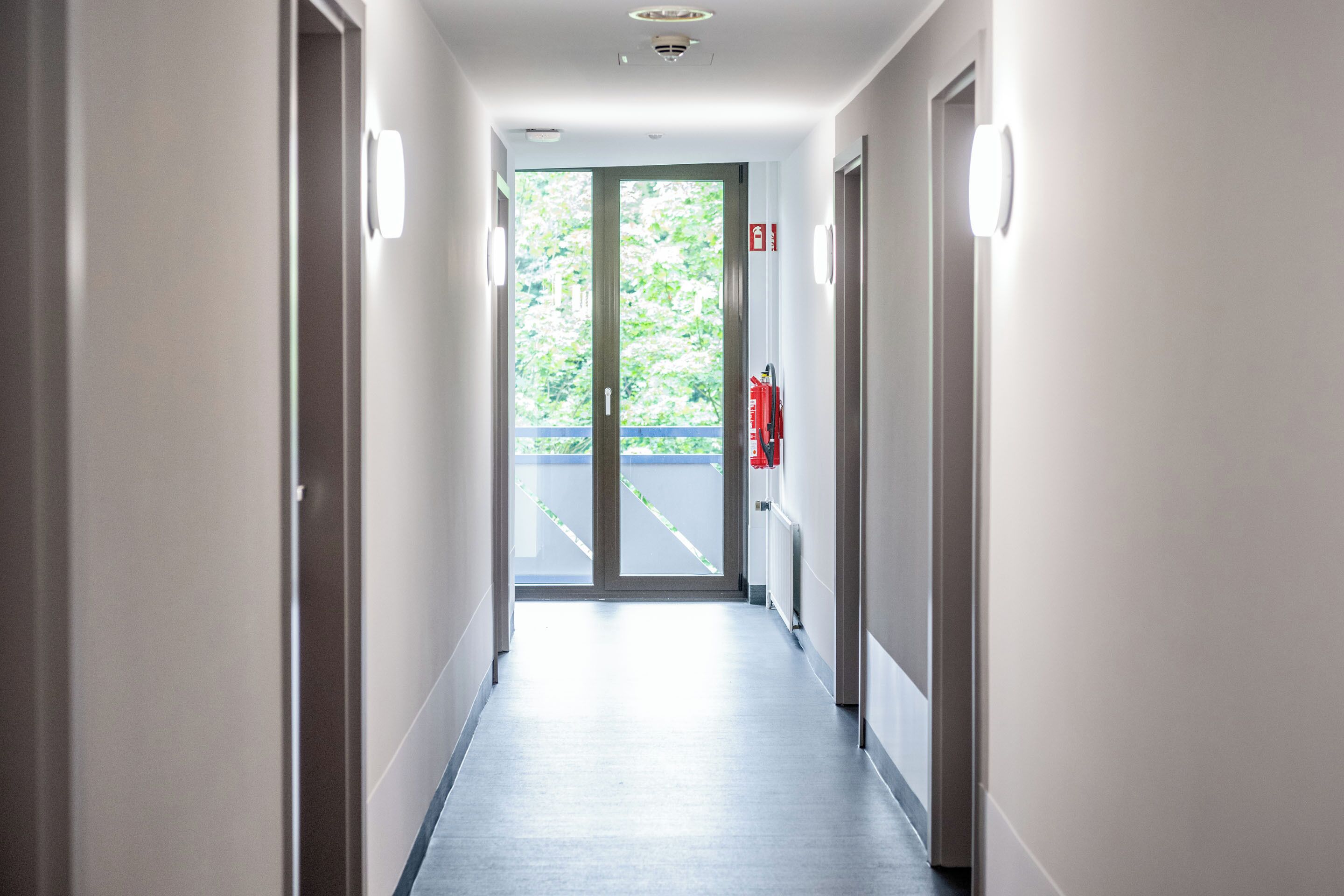 A long, narrow hallway with doors on both sides, leading to a glass door at the end.
