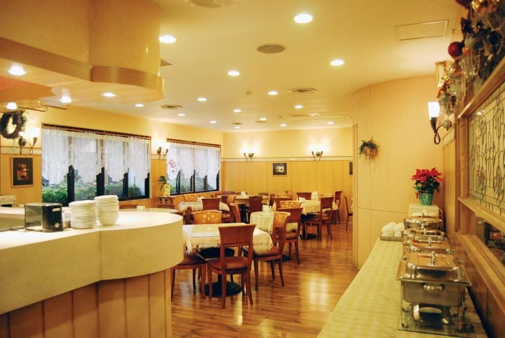 A hotel dining area with round tables, chairs, and buffet stations.