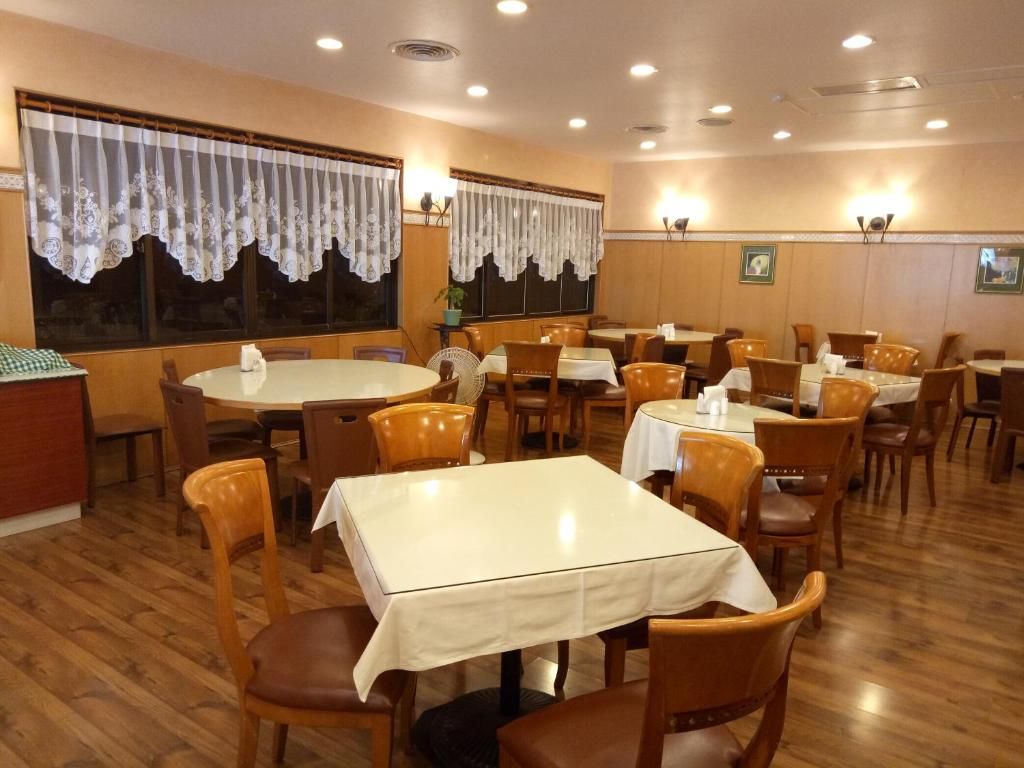 A restaurant with round tables and chairs, wooden floors, and curtains on the windows.