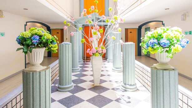 Un pasillo con piso a cuadros, altas columnas y plantas en macetas con flores.