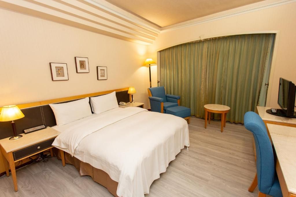 A hotel room with a bed, bedside tables, a desk, a chair, a television, and a curtain.