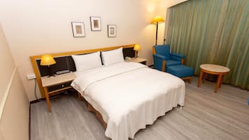 A hotel room with a bed, bedside tables, a desk, a chair, a small round table, and a curtain.