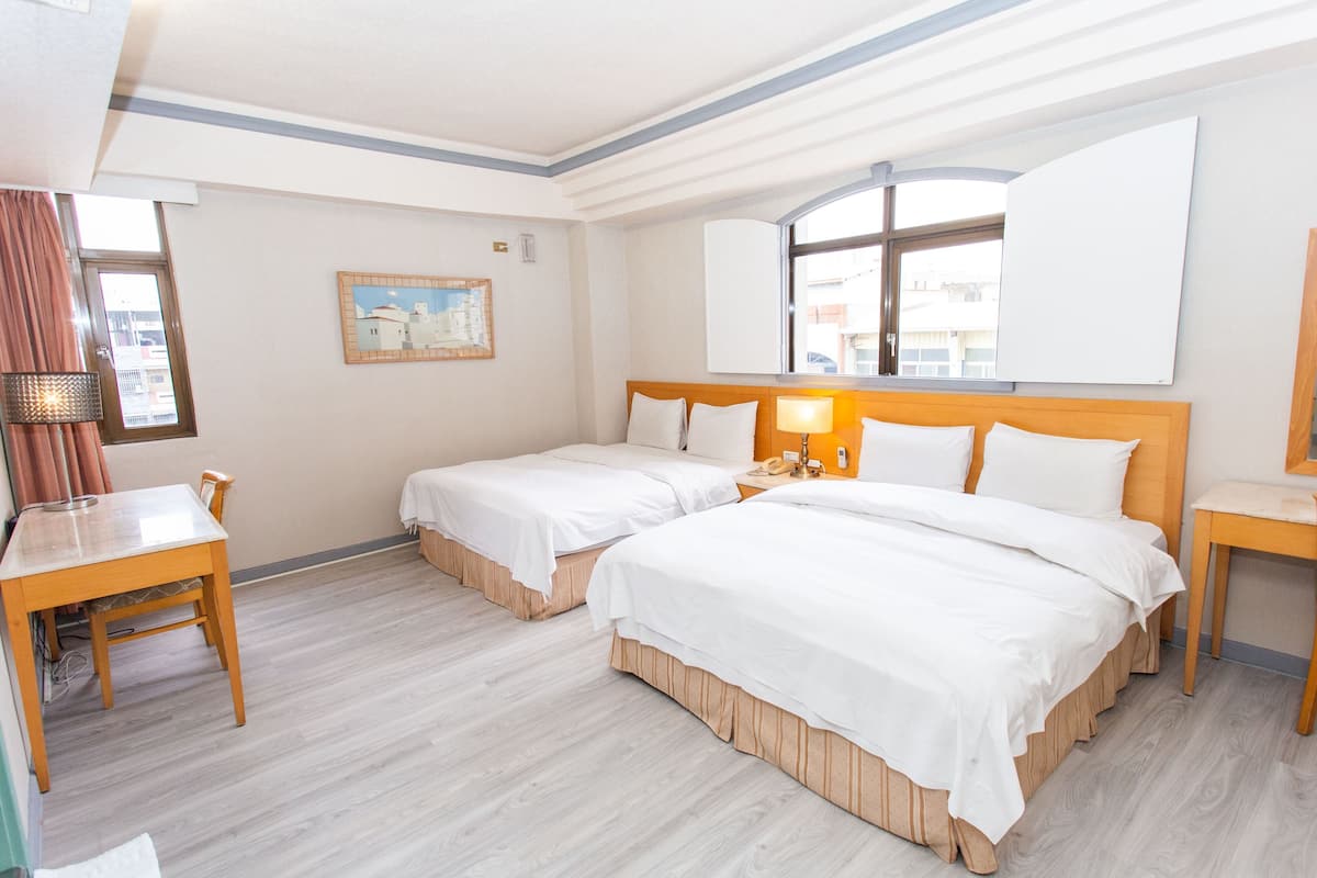 A hotel room with two beds, a wooden table, a desk, a lamp, and a painting on the wall.