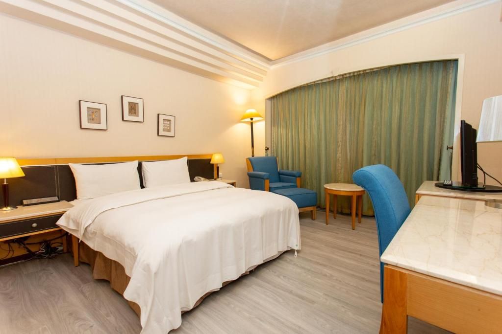 A hotel room with a bed, a desk, a chair, and a television.