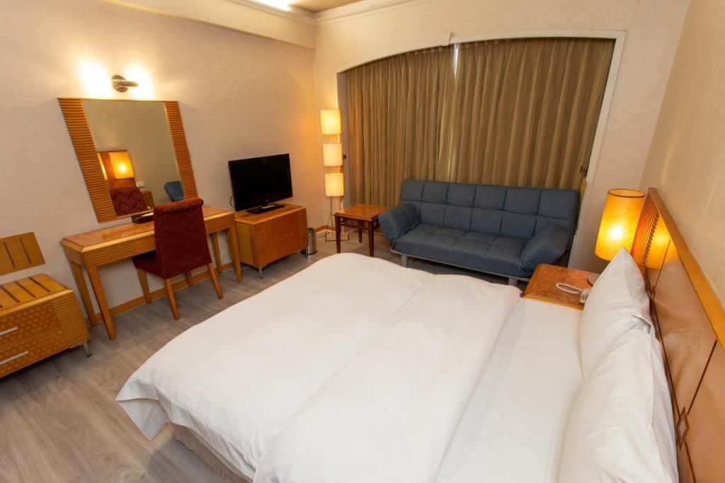 A hotel room with a bed, a desk, a chair, a television, and a sofa.