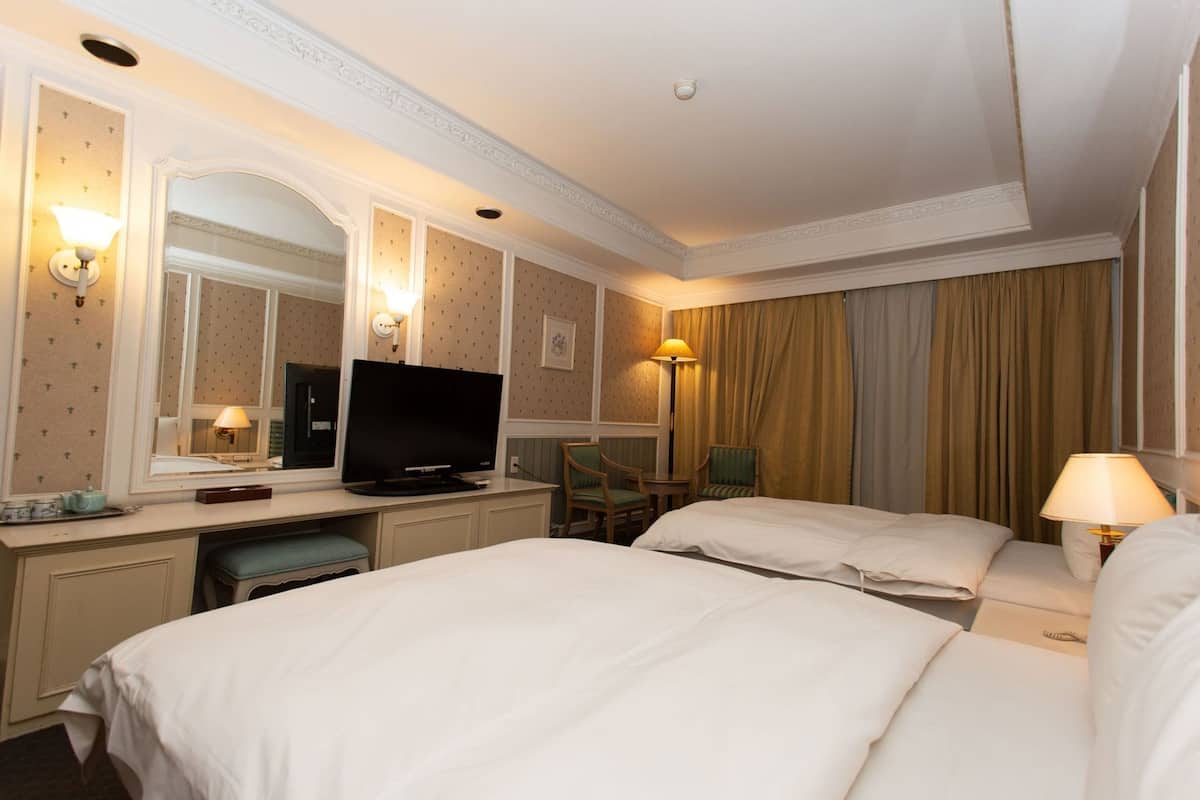 A hotel room with two beds, a desk with a television, a chair, and a lamp.
