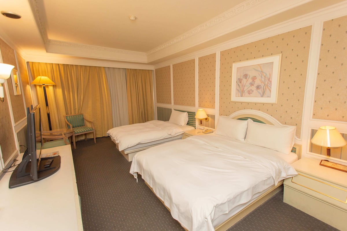 A hotel room with two beds, a desk with a computer, a chair, and a painting on the wall.