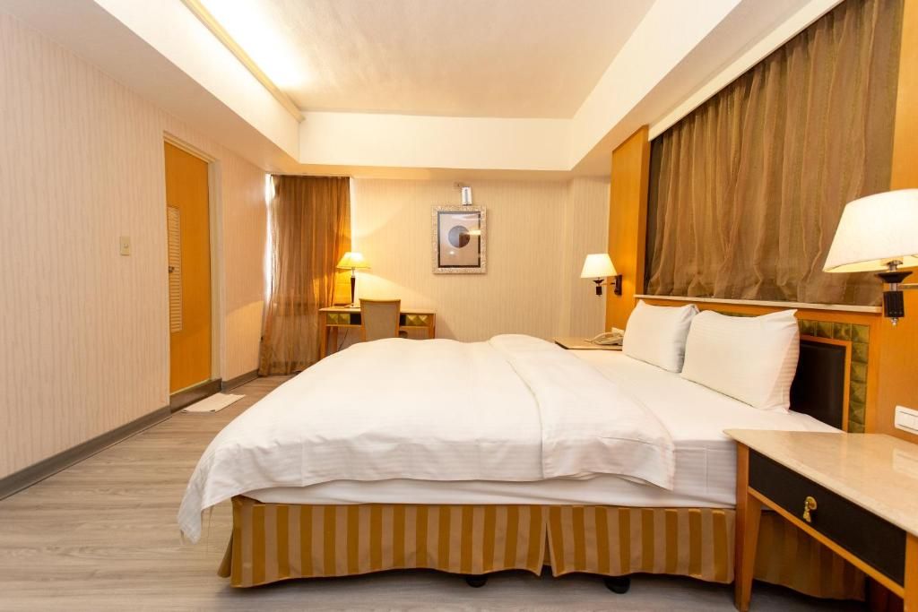 A hotel room with a large bed, bedside tables, lamps, a mirror, and a door.