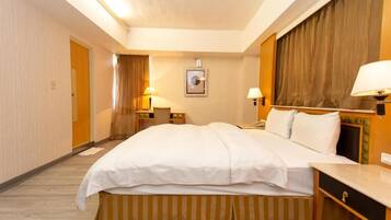 A hotel room with a large bed, bedside tables, lamps, a mirror, and a door.