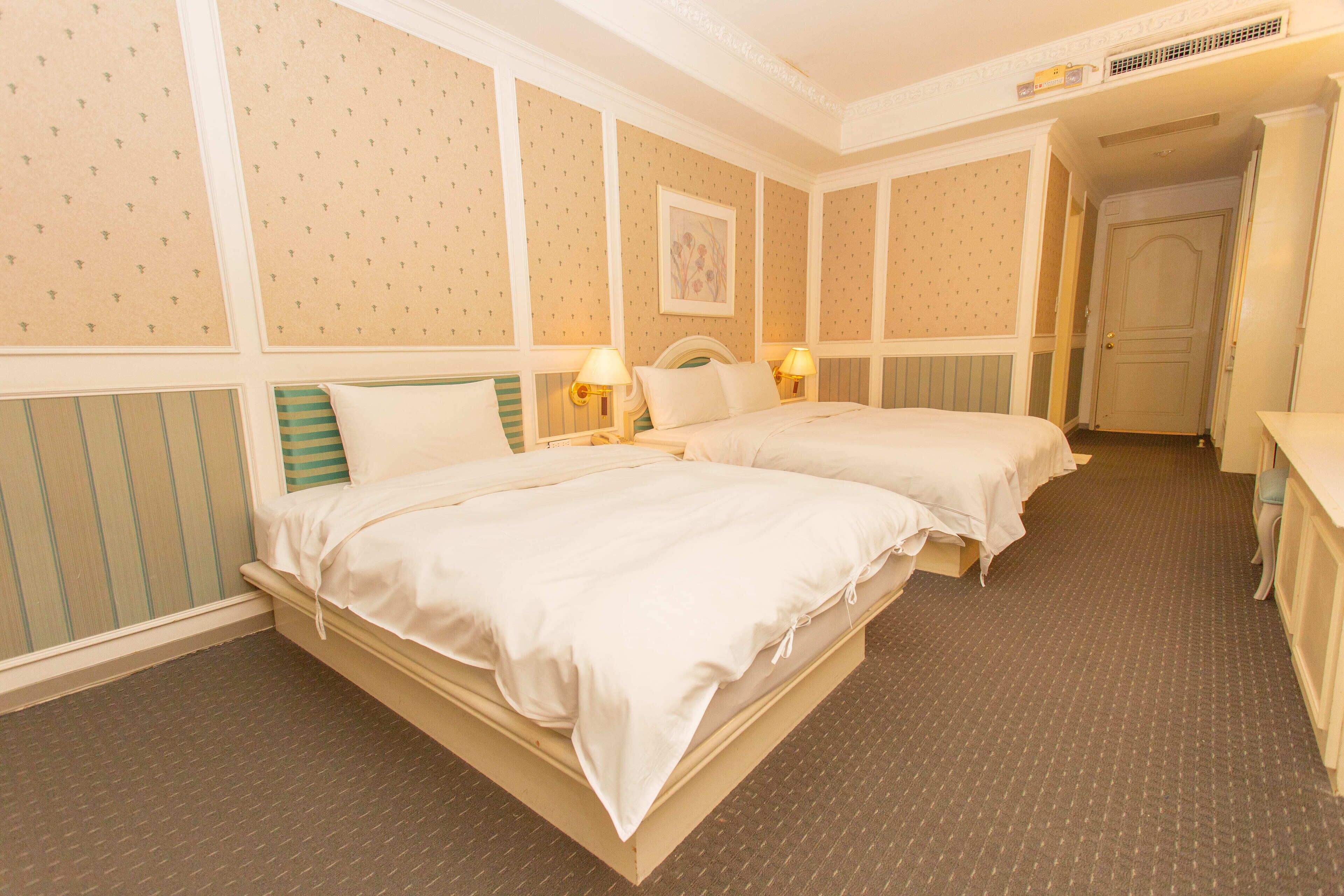 A hotel room with two beds, a dresser, and a door leading to another room.