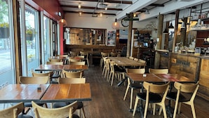 A restaurant interior with wooden tables and chairs, a bar area, and a view through large windows. - Akureyri Backpackers (Akureyri)