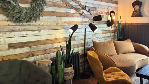 A cozy living room with a wooden wall, a green couch, a yellow armchair, and a fireplace. - Akureyri Backpackers (Akureyri)