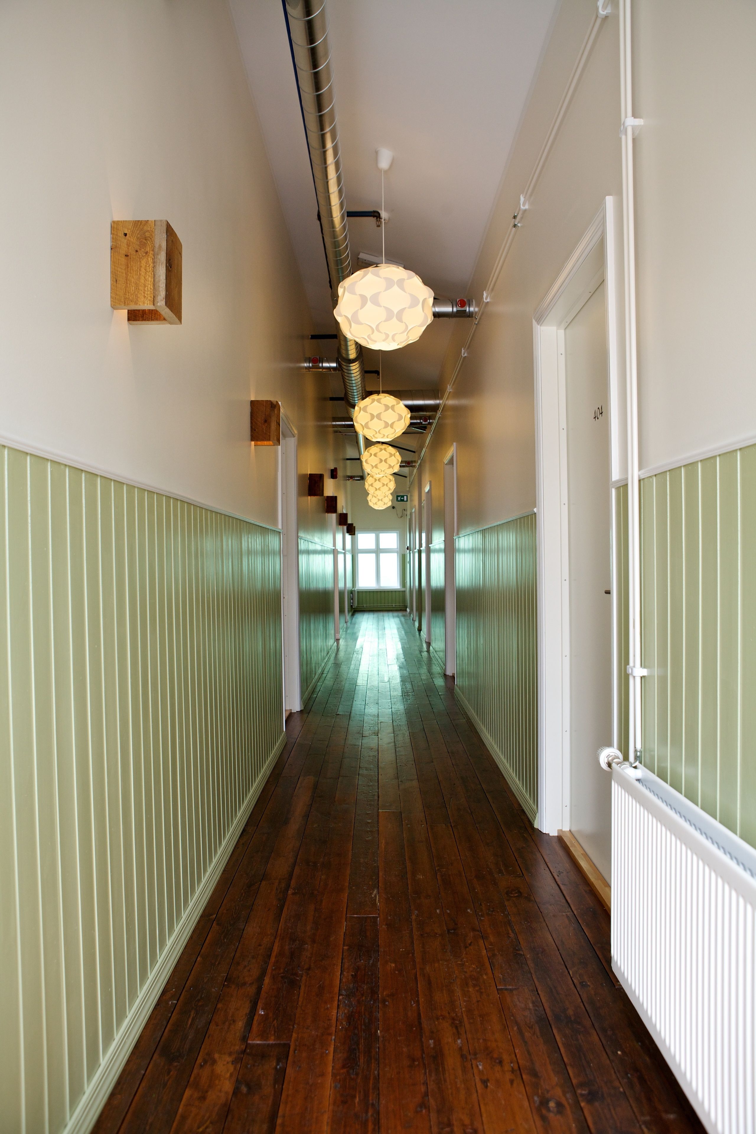 A long hallway with wooden flooring, green wainscoting, and white doors.