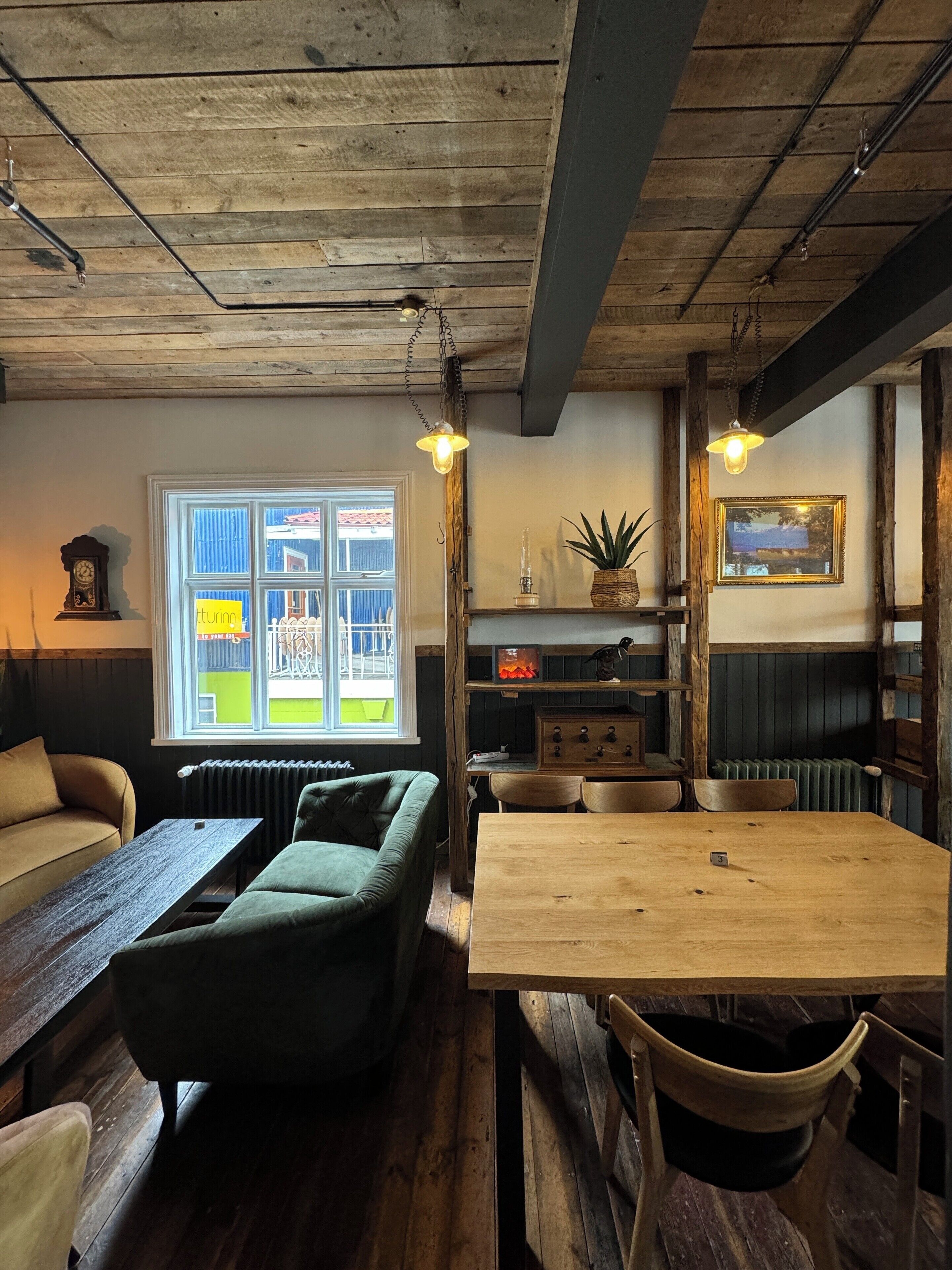 A rustic room with a wooden table, green sofa, and a window with a view of a building.