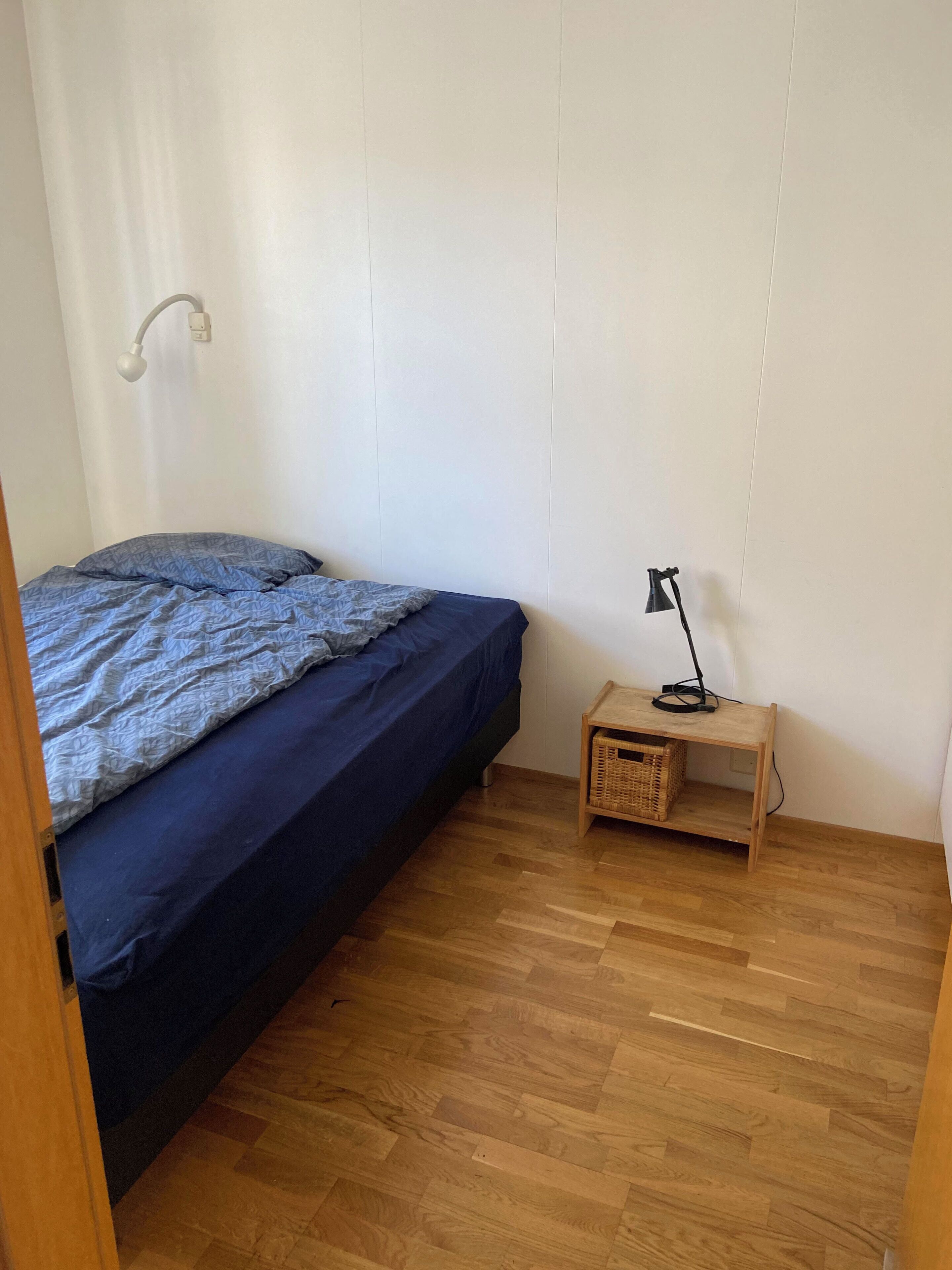 Un dormitorio pequeño y ordenado con una cama individual, una mesita de noche, una lámpara y suelo de madera.