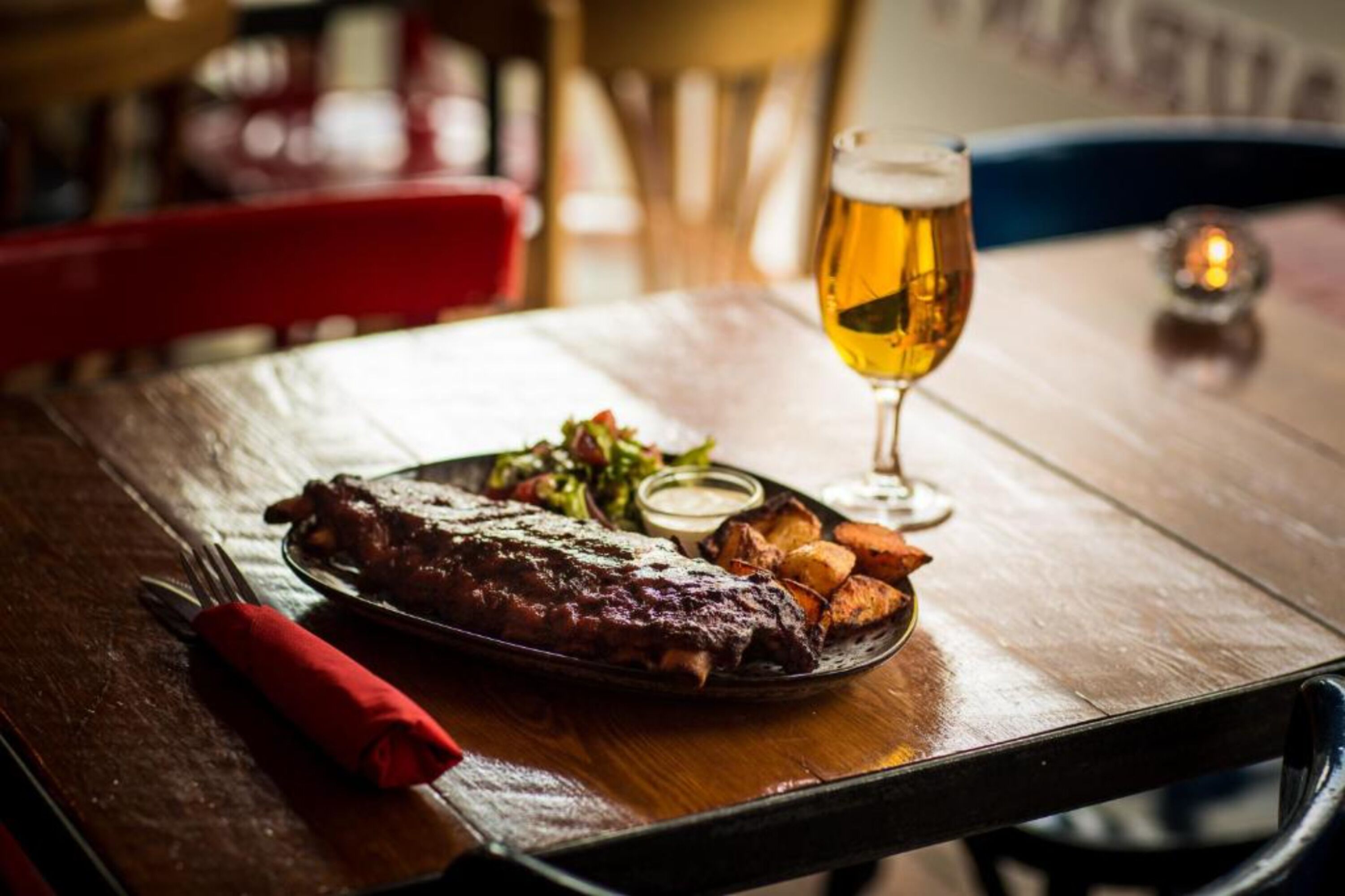 Une table à manger avec une assiette de nourriture, un verre de bière et une serviette rouge.