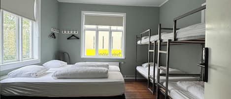 A dormitory room with bunk beds, a window with a view, and a ceiling light.