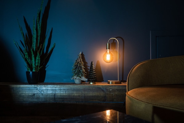 A cozy living room with a modern sofa, a potted plant, and a table lamp.