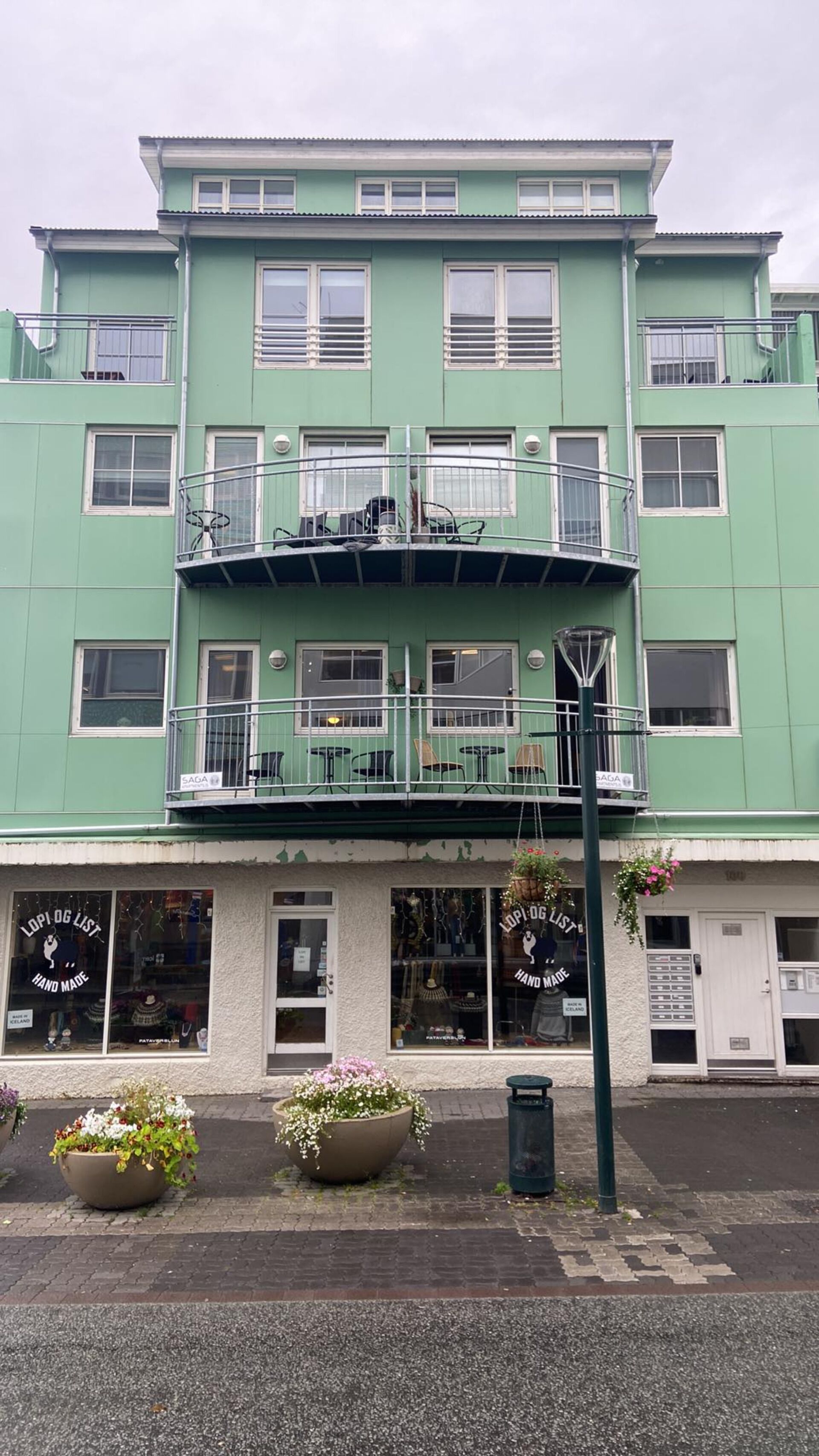 A two-story building with a green facade, multiple windows, and a balcony with outdoor seating.