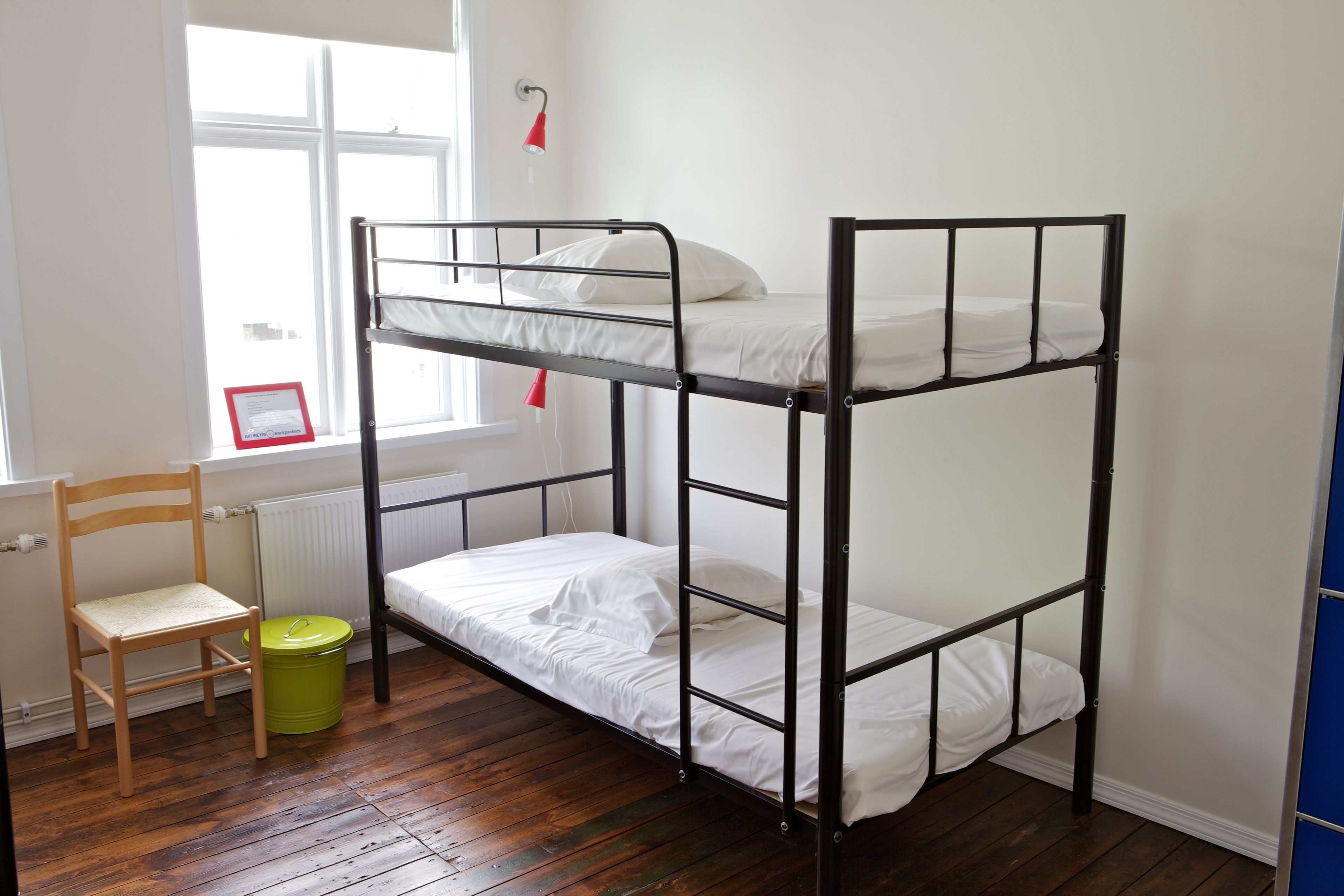A bunk bed room with a wooden chair and a green trash bin.