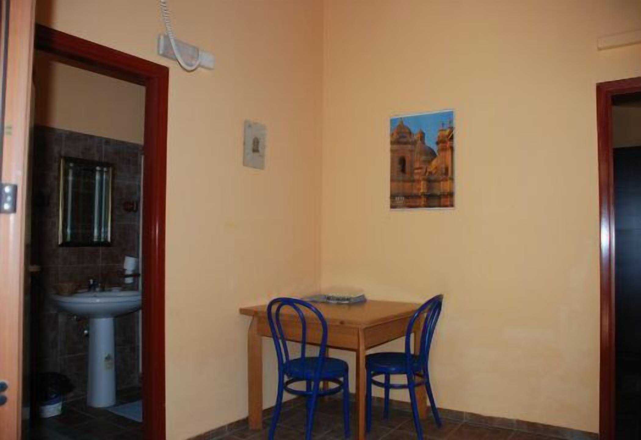Una habitación pequeña con una mesa de madera y dos sillas azules, un teléfono de pared y una fotografía de un edificio.