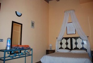 Relax in a classic room with a bed under a canopy, bedside table, and a small table with a unique lamp.