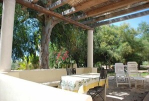 Un patio al aire libre con mesa y sillas, rodeado de follaje y árboles.
