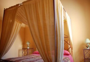 Ein Himmelsbett mit rosa Bettdecke und Kissen, zwei Nachttische mit Lampen und ein Holz-Kopfstück.