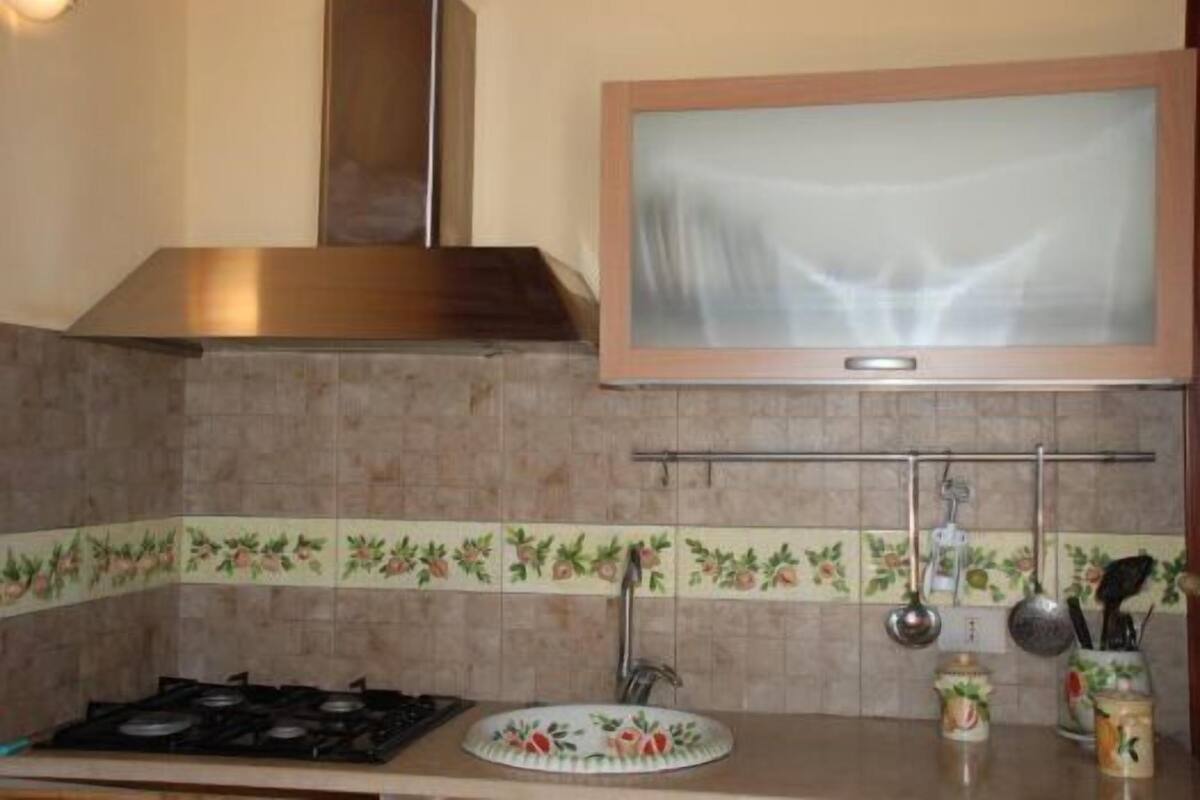 Uma cozinha com fogão a gás, coifa de aço inoxidável, televisão na parede e painel de azulejos com motivos de frutas.