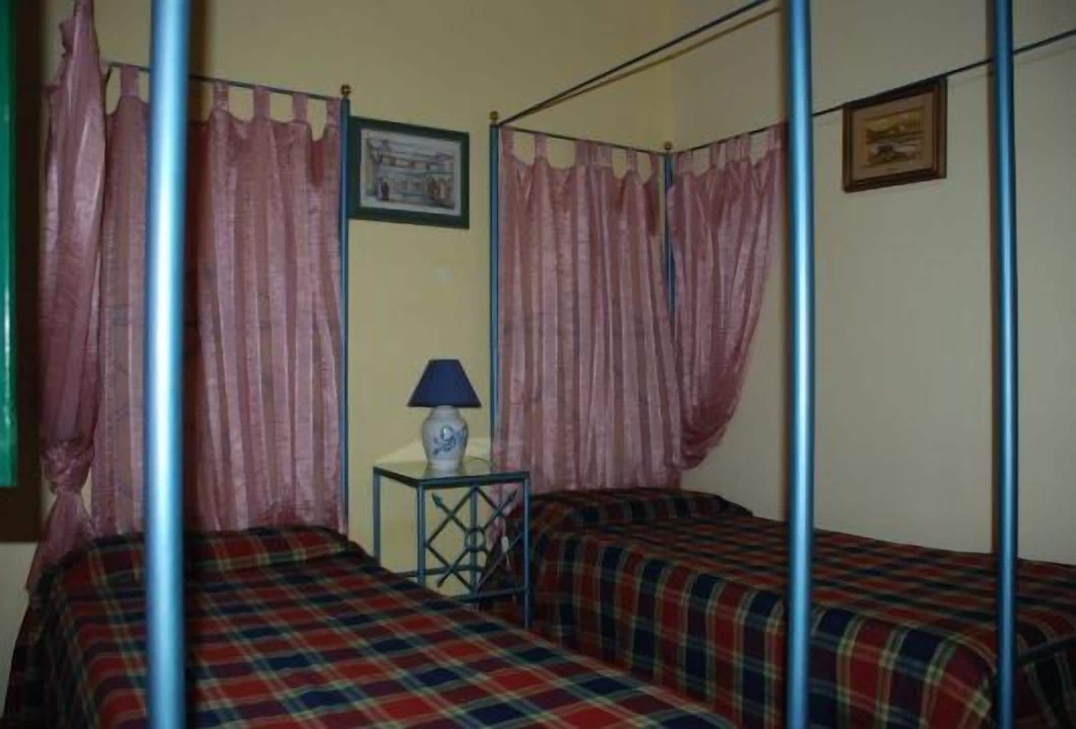 A room with a four-poster bed, a small bedside table with a lamp, and a framed picture on the wall.