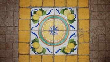 Een betegelde muur met een centrale decoratieve tegel met een bloemmotief en vier kleinere tegels met citroenmotieven.
