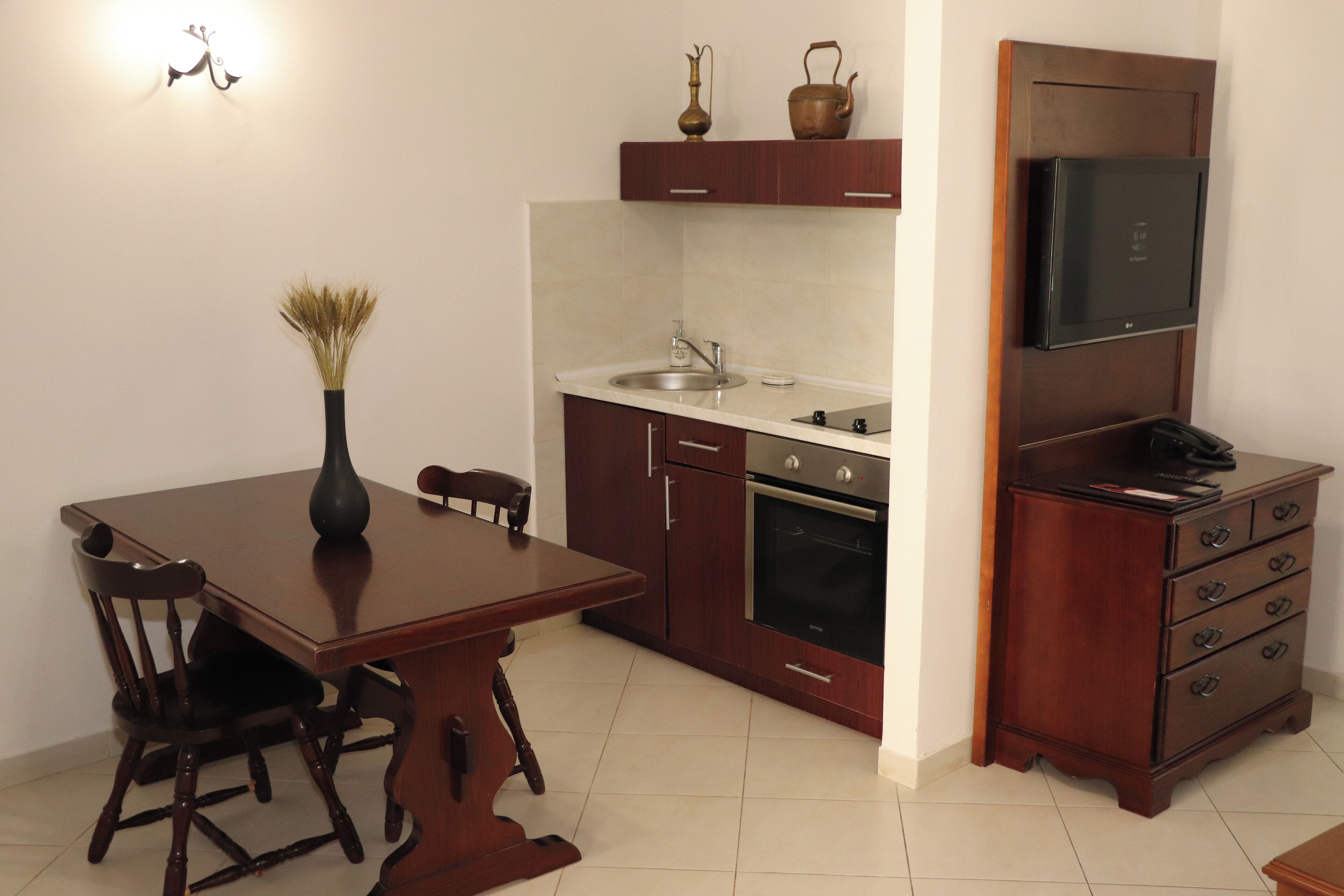 A compact kitchen with a wooden table, chairs, a sink, a stove, and a built-in oven.