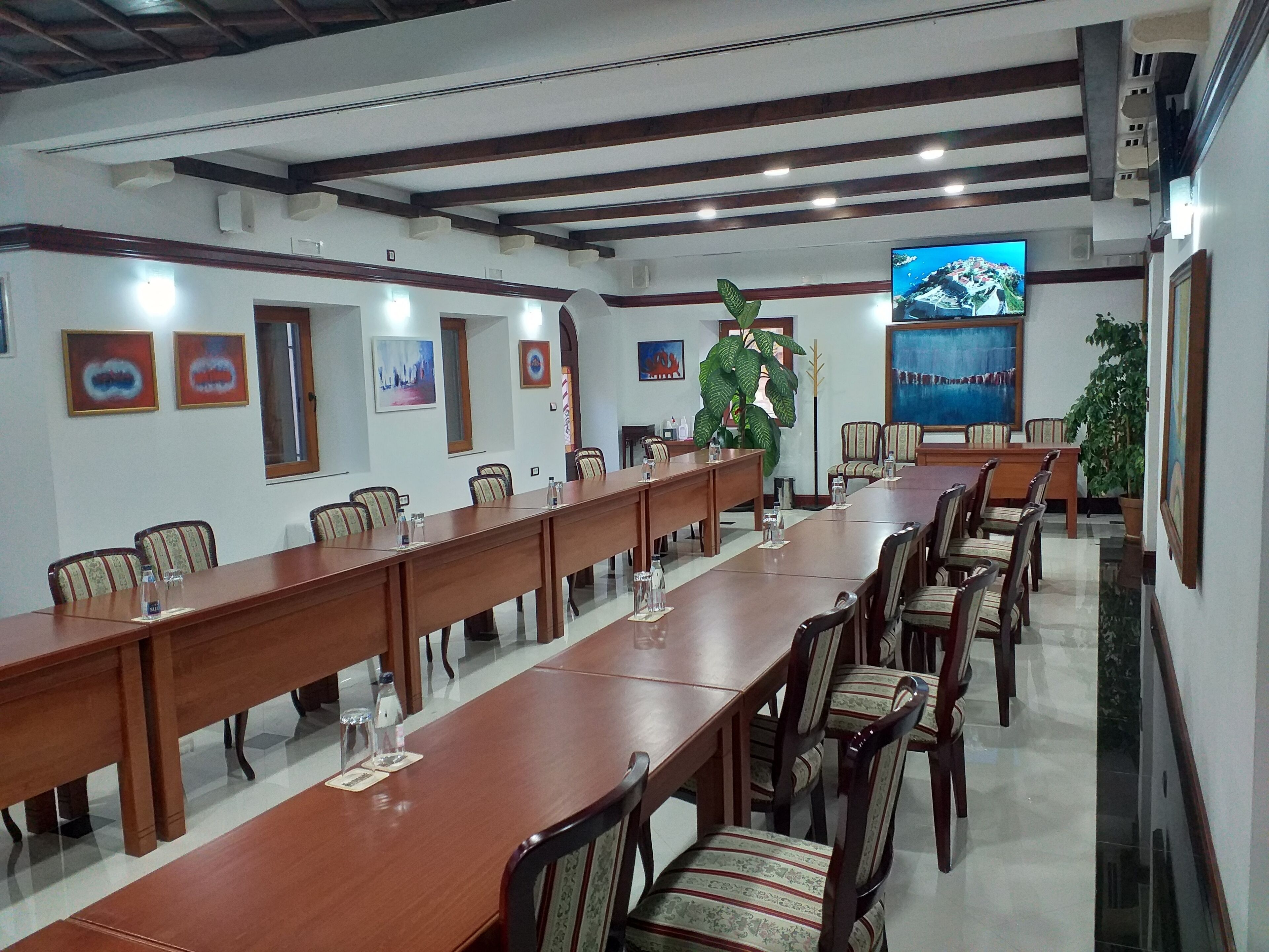 A conference room with long tables and chairs, a large TV screen, and framed artwork on the walls.