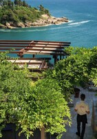 Vista de una zona costera con una terraza de madera que da al mar, rodeada de vegetación.