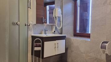 Un baño moderno con cabina de ducha de vidrio, un lavabo blanco con mueble de madera, un inodoro y una ventana que proporciona luz natural.