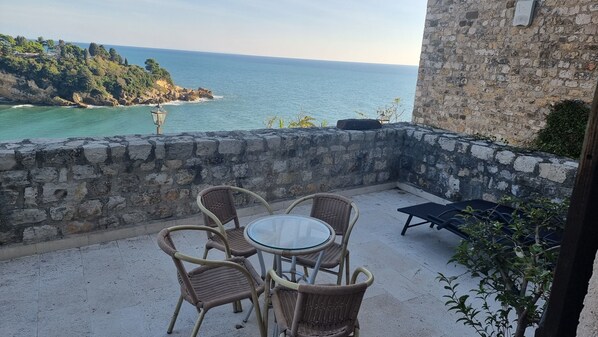 A balcony with wicker chairs and a glass table overlooking a coastal view.