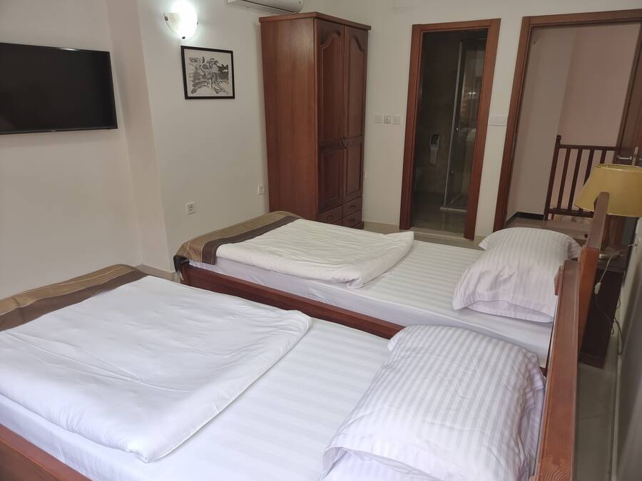 A hotel room with two beds, a wardrobe, a television, and a door leading to a bathroom.