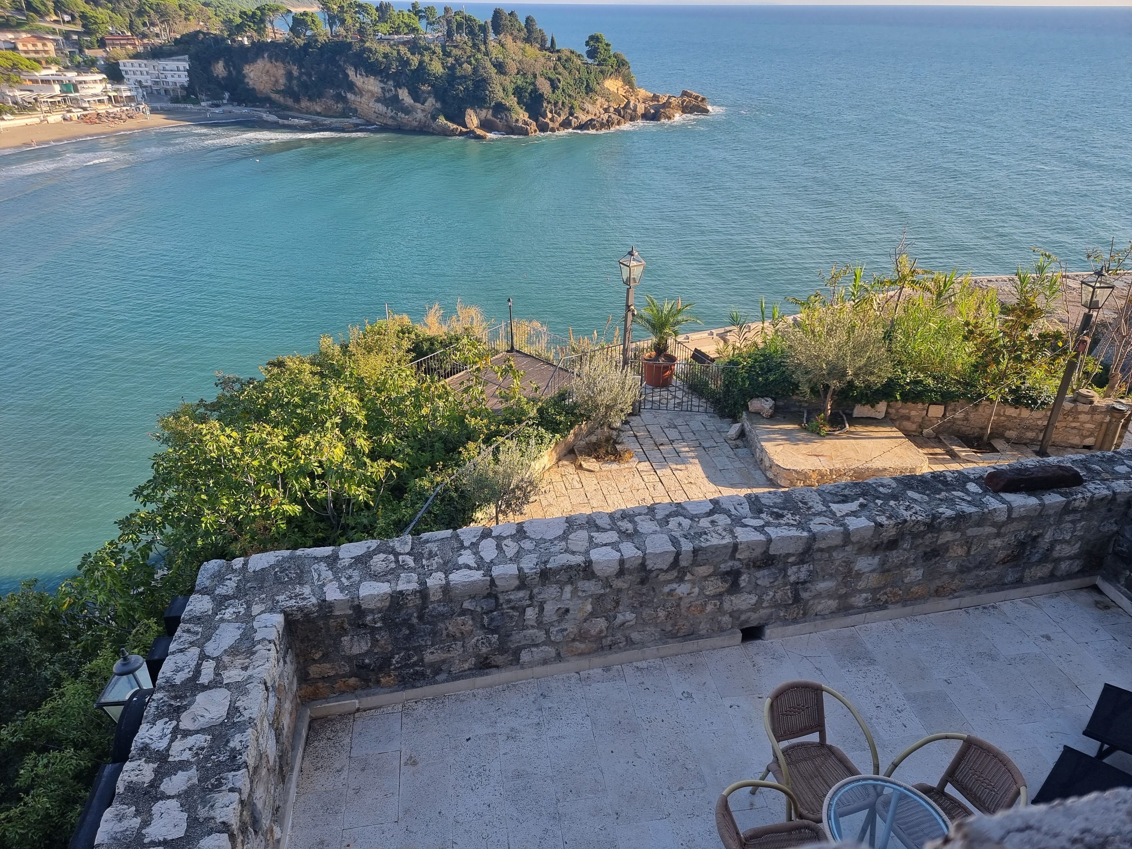 A coastal view with a stone wall, outdoor seating, and a view of the sea and a small island.