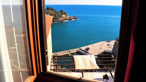 A view from a window overlooking a coastal area with a clear blue sea, a rocky shoreline, and a building with a sloped roof. - Palata Venezia (Ulcinj)