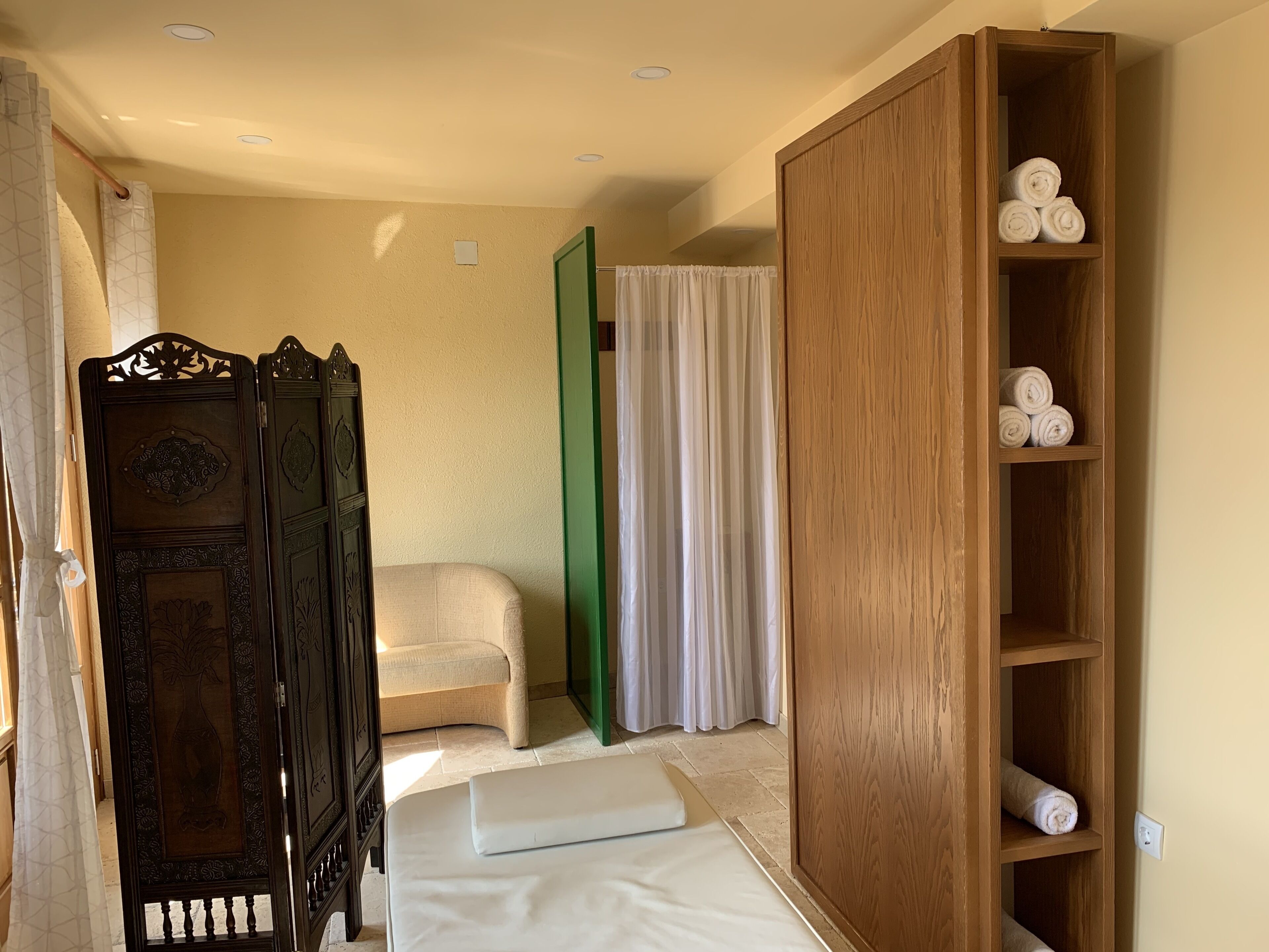 A room with a bed, a wooden wardrobe, a green door, and a shelf with rolled towels.