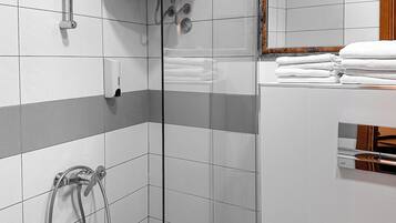 Et moderne badeværelse med en glasbrusekabine, toilet og en stak hvide håndklæder.