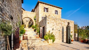 A stone building with a staircase leading to a door, surrounded by potted plants and a statue. - Palata Venezia (Ulcinj)