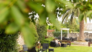 An outdoor seating area with black chairs and tables, surrounded by greenery and a palm tree. - Hotel Finca Alcamino (Santa Cruz de Bezana)