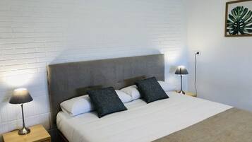 A neatly made bed with a headboard, two bedside lamps, a wooden nightstand, and a framed plant on the wall.