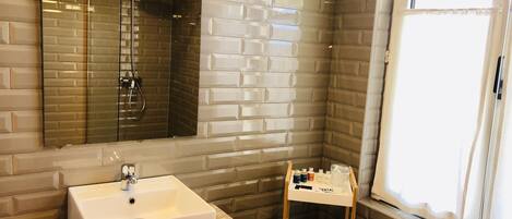 Un baño con lavamanos blanco, espejo, ducha y ventana.