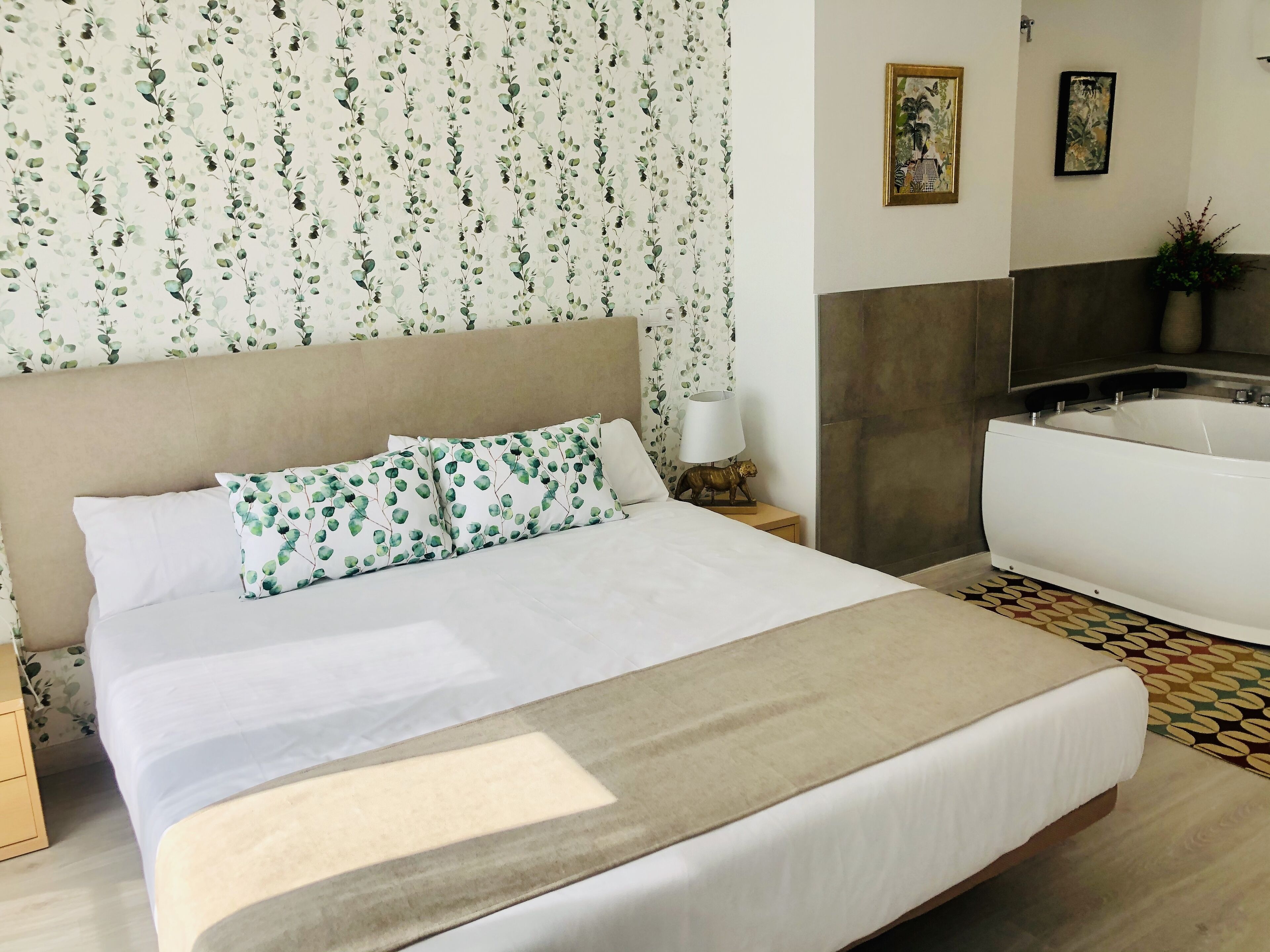 A hotel room with a bed, a nightstand with a lamp, a sofa, and a bathroom with a bathtub.