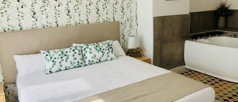 A hotel room with a bed, a nightstand with a lamp, a sofa, and a bathroom with a bathtub.