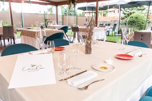 Un espacio exterior con mesas preparadas para una comida, incluyendo copas de vino, platos y cubiertos.